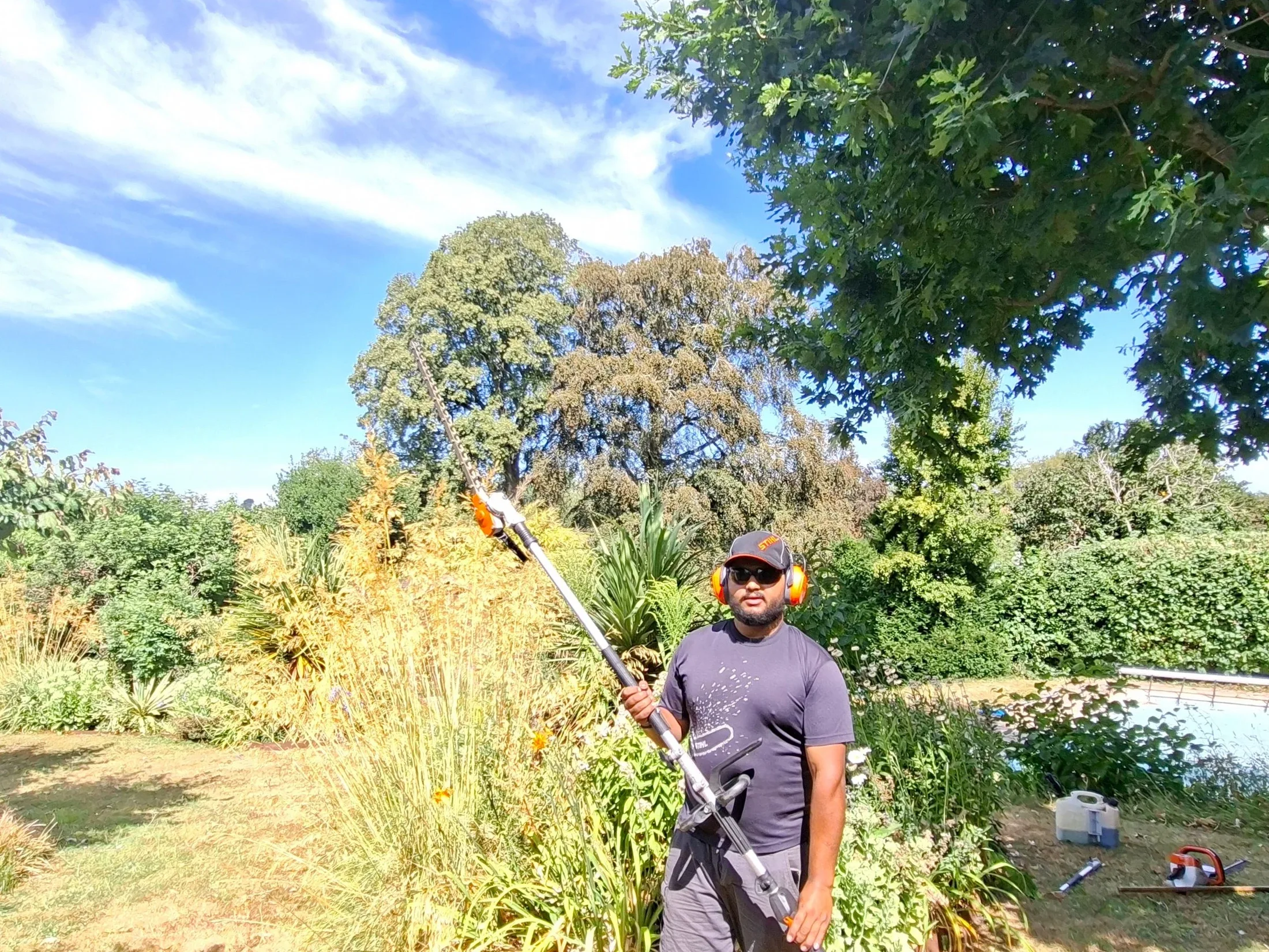 Rafi working in a local garden with a long-reach hedge trimmer.